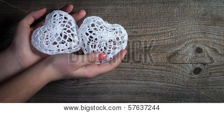 Woman hands holding white lace hearts on old wood background.