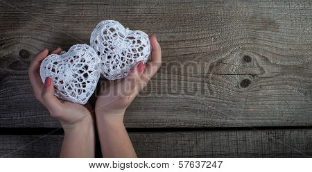 Woman hands holding white lace hearts on old wood background.