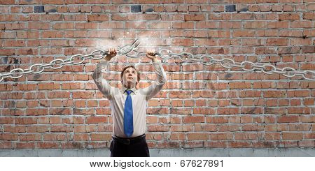 Young furious businessman breaking metal chain with hands