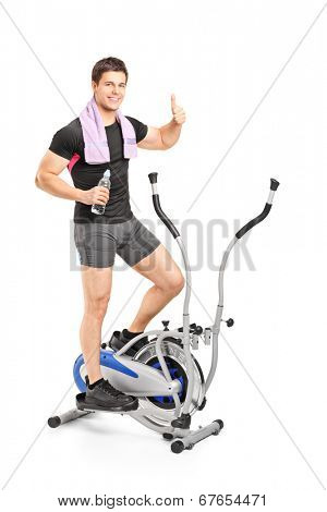 Full length portrait of a young guy exercising on a cross trainer machine isolated on white background
