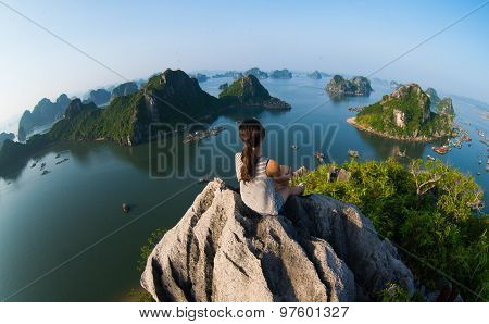 A young traveler girl sit on the top of mountain in Halong bay and enjoy the beauty of seascape.