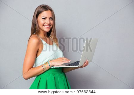 Smiling cute girl using laptop over gray background and looking at amera