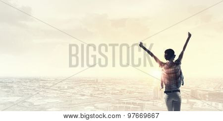 Rear view of girl with hands up facing sunrise abone city