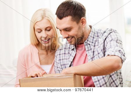 people, delivery, shipping and postal service concept - happy couple opening cardboard box or parcel at home