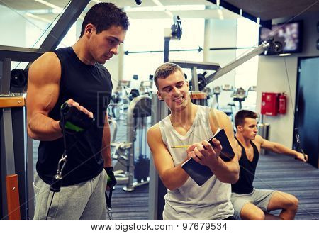 sport, fitness, lifestyle and people concept - men with clipboard taking notes and exercising on gym machine