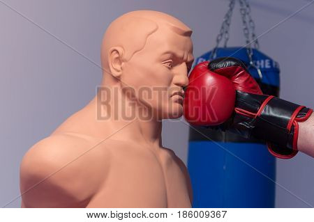 Red boxing gloves punching a dummy mannequin doll on a gym with a blue punching bag on the background