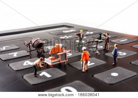 fixing the problem concept closeup of miniature figurine of workers reparing number buttons on a big black calculator