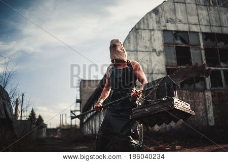Mutant monster with weapon in form of hammer saw and an ax. Imagination. Mutant with sack on his head.