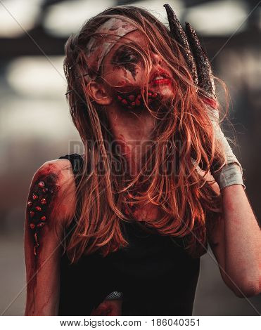 Mutant girl portrait in wounds and ulcers with nails in her head and claws instead of fingers. On her head and hands is bandage.