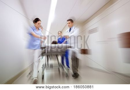 health care, reanimation and medicine concept - group of medics or doctors carrying unconscious woman patient on hospital gurney to emergency (motion blur effect)