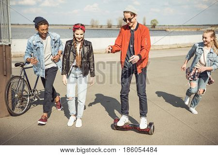 stylish hipster boy riding gyroboard with friends near by teenagers having fun concept