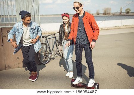 stylish hipster boy riding gyroboard with friends near by teenagers having fun concept
