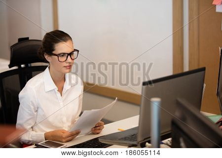 Young businesswoman reading documets while sitting at desk in office