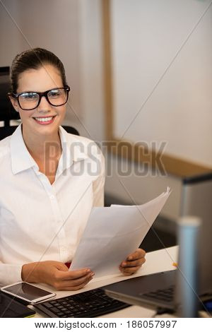 Portrait of smiling businesswoman holding documets at desk in office