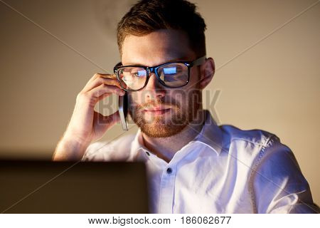 business, overwork, people, deadline and technology concept - businessman in glasses with laptop computer calling on smartphone at night office