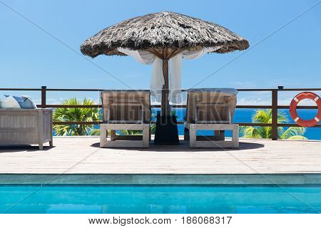 travel, tourism, vacation and summer holidays concept - palapa and sunbeds at seaside swimming pool