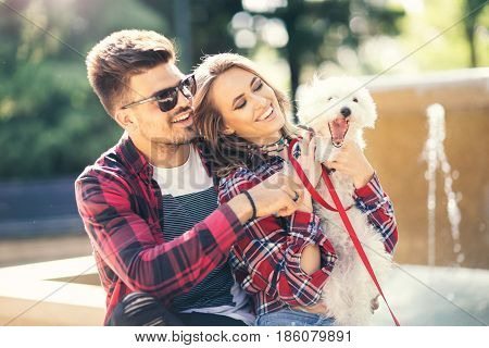 Young couple with puppy. Portrait of attractive happy smiling young woman and man holding cute little dog summer park outdoor.