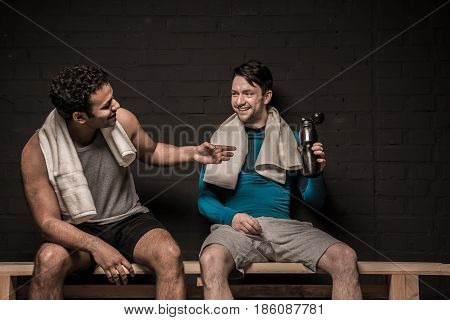 Handsome male athletes resting and conversing at gym locker room