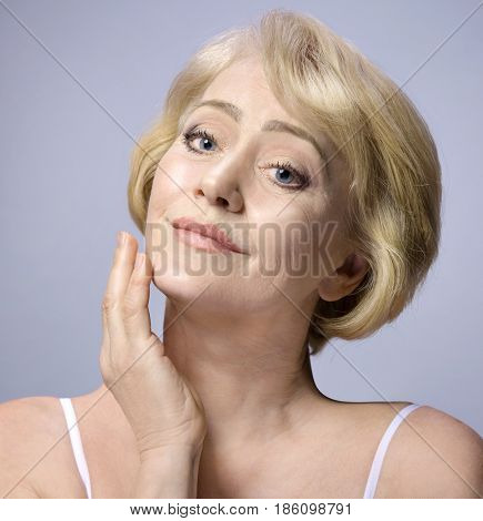 Beautiful Matured Woman Touching her Face with hand. cheerful caucasian smiling blond. Studio shot. Looking off camera. Facecare. Grey background. 50 . Skin care concept
