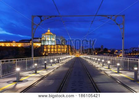 Empty tram rails on the Dom Luis I or Luiz I iron arch bridge across Douro river and Monastery of Serra of Pilar in Porto during morning blue hour, Portugal.