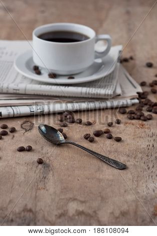 A cup of black coffee on a wooden table with grains and newspaper a gray toning. Black Coffee Grain Newspaper Wooden Background Retro Photo Breakfast