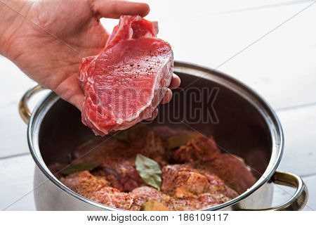 Close up of chefs hands spicing the meat. Casserole with raw meat on a white background.