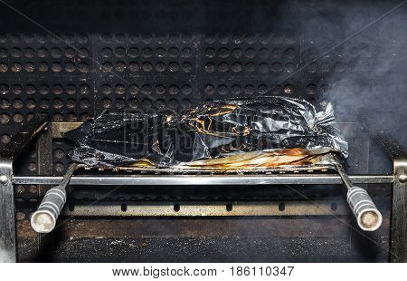 Roasting a Tambaqui fish wrapped on a laminated paper on a barbecue grill.