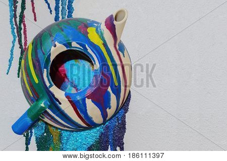 Old multicolor painted teapot is attached on the vertical white cement wall with copy space close-up