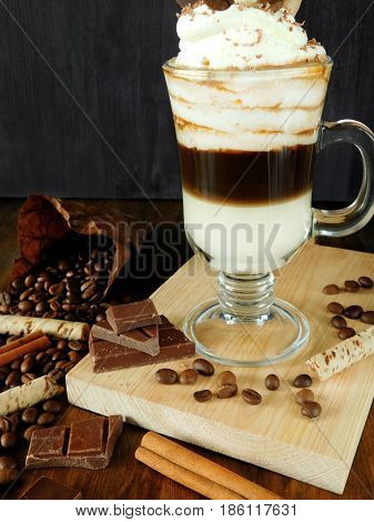 Coffee cocktail with whipped cream in an Irish coffee mug surrounded by coffee beans, cinnamon and chocolate bars