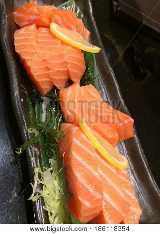 Special Deluxe salmon sashimi set with slice lemon and green seaweed on black plate traditional Japanese healthy foodRaw salmon with fat selective focused with blur background
