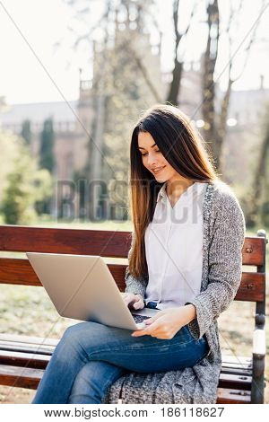 Portrait Of A Young Professional Woman Using A Laptop Computer While Sitting On A Bench In A Park, O