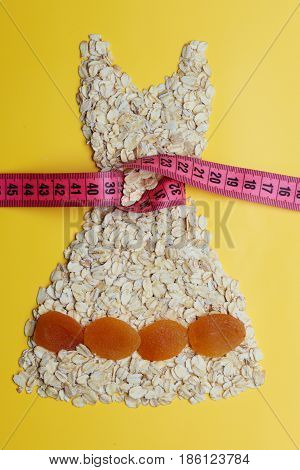 Dieting healthy eating slim down concept. Female dress shape made from oatmeal dried fruit with measuring tape around thin waist on yellow