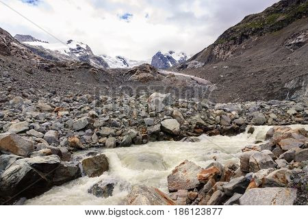 Wild river of the melting water of the Morteratsch and Pers glacier in the Rhaetian alps on a cloudy day in the summer. Morteratsch Engadin Grisons Switzerland