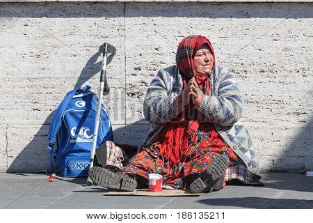 ROMA, ITALY. March 11, 2016: Homeless beggar. Woman asking for alms in street in Rome Italy. An elderly woman with her hands folded in prayer is sitting in the middle of the street to passersby.