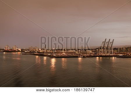 Auckland New Zealand - March 6 2017: Overview of the commercial harbor at sunset with container terminal and ships. Lights on the docks reflected in the water.