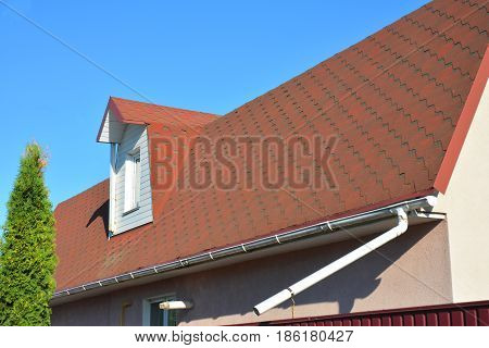 Roof Asphalt Shingles with Moss. Rain Gutter Pipeline with Downspout Pipe and Attic Mansard Window. Roofing Construction Roofing Repair.
