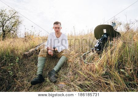 Dyatlovichi, Belarus - October 1, 2016: Reenactor Dressed As Russian Soviet Red Army Soldier Of World War II Sitting Near Maxim Machine Gun Weapon In Ambush In Autumn Meadow At Historical Reenactment