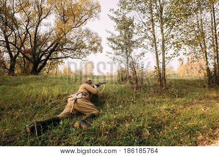 Dyatlovichi, Belarus - October 2, 2016: Reenactor Dressed As Russian Soviet Red Army Soldier Of World War II Hidden Sitting And Aiming Rifle Weapon In Grass In Autumn Forest