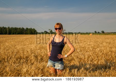 A young beautiful woman standing at wheat field under sunlight.