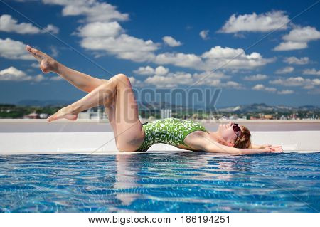 A young beautiful girl lying on the edge of the pool with сloudy sky on the background