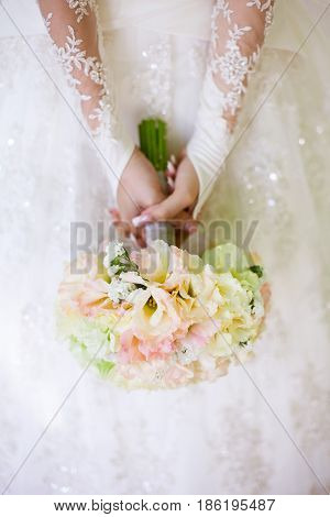Bride in a beautiful white lacy wedding dress holding a flowers bouquet from white fresh rose in hands. Wedding bridal bouquet close up. Tenderness, love, wedding, fashion - concept.
