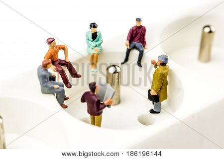 closeup of miniature figurines having a meeting close to an electricity switch button multiplug on white background