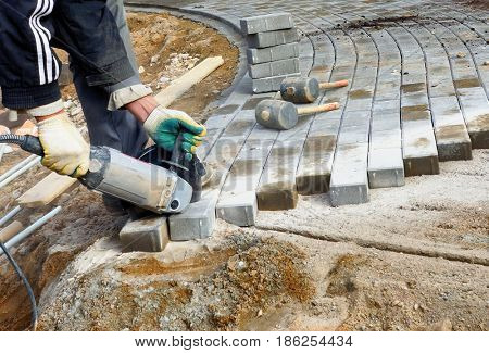 A man saws an electric saw with a paving slab, repairing a stone path.