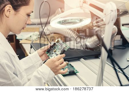 Beautiful female computer expert professional technician examining board computer in a laboratory in a factory. Troubleshooting. Technical support.