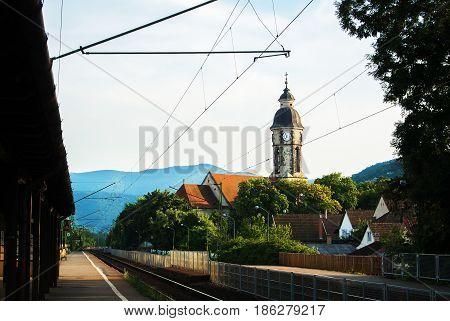 Small Railway Station, A Tower With Clock, Houses With Tile Roofs And Mountains At The Background, N