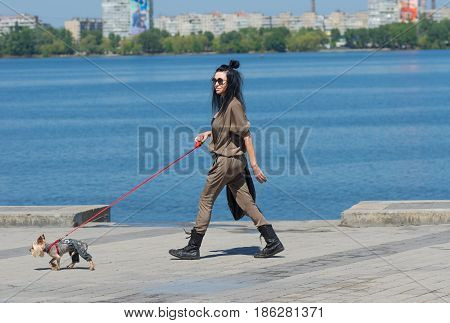 Dnipro Ukraine - May 06 2017: Dandy Yorkshire Terrier dog wearing jeans leads fashionable woman on a Dnepr river embankment in Dnepr city Ukraine