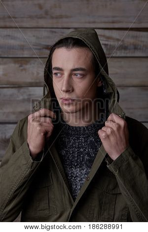 Handsome man wearing green jaket and torn jeans in wooden rural house interior