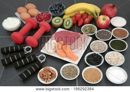 Large health food collection for body builders with dumbbell weights and hand grippers on slate background.