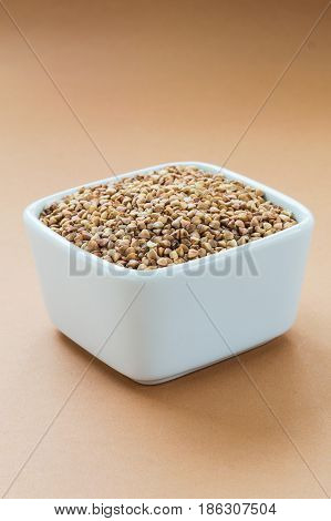 Raw organic buckwheat in white bowl on bright brown background. Superfood vertical