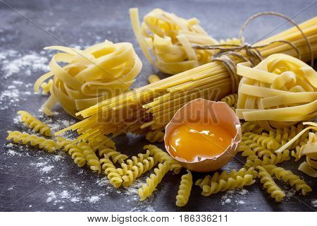Different Kinds Of Pasta Spaghetti, Fusilli, Fettuccine And Raw Egg Yolk On The Kitchen Wooden Table